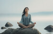 © SnapVault - A young woman meditating on a rock at the seashore on the beach, practicing mindfulness and focused breathing to improve her mental well-being.breathwork concept