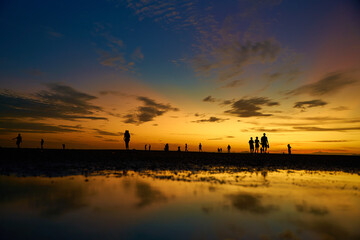 Wall Mural - Silhouettes of people walking on the ocean floor after the evening tide. Incredible colors of the evening sky