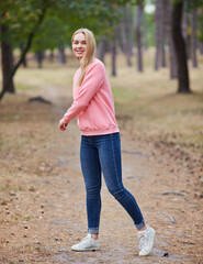 Wall Mural - Attractive blue eyed blonde woman walk on the city park. Girl wear pink hoodie, pink bag and look happy and smiles.