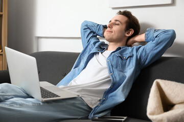 Male freelancer with laptop resting on sofa at home