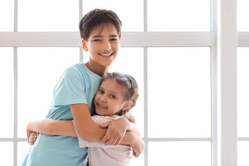 Wall Mural - Little boy hugging his sister near window