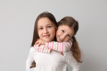 Wall Mural - Cute little sisters hugging on light background