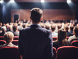 © B & G Media - A speaker addressing an audience in an auditorium during a seminar, viewed from behind, showcasing the educational interaction.