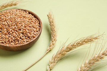 Wall Mural - Wooden bowl with grains and wheat ears on light green background