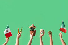 Female Hands Holding Mexican Flags, Cactus, Painted Skull, Chilli Peppers And Limes On Green Background