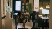 African American Employees Having Fun At Work During Nightshift, Holding Race With Desk Chairs. Relaxed Coworking Businessmen Enjoying Overnight Stay In Office, Playing Together