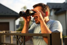 Concept Of Private Life. Curious Man With Binoculars Spying On Neighbours Over Fence Outdoors