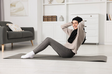 Wall Mural - Muslim woman in hijab doing abs exercise on fitness mat at home