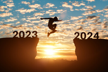 Happy new year 2024 concept. Silhouette of man jump on the cliff between 2023 to 2024 years over sunset or sunrise background.