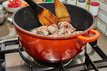 Wall Mural - Pieces of beef are fried in pan on gas stove. Wooden sticks for stirring