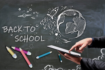 Poster - Close up of businessman hand holding and pointing at tablet with abstract back to school sketch with pencils and rocket on chalkboard wall background. Education and knowledge concept.