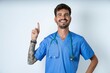 © Roquillo - young caucasian doctor man wearing blue medical uniform holding finger up having idea and posing