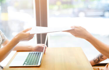 Hands in close-up pass documents to each other above the table with the laptop. Business work, interview, subsidy, lease agreement, agreement. A young man hands over documents for signature