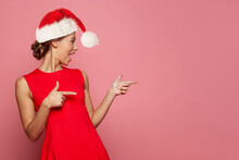 Christmas Portrait Of Happy Woman Santa Pointing And Having Fun Against Bright Pink Color Studio Wall Background