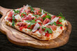 Sorrentina pizza with prosciutto, arugula, capers, pelati sauce, pesto. Roman pizza rectangular on wood background