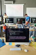 © Mediaphotos - Vertical image of computer with codes on monitor standing on desk in the classroom with students and teacher in background