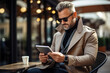 © Sergio - Adult stylish business man in suit raincoat and sunglasses using tablet while sitting in cafe, caucasian businessman working online outdoors