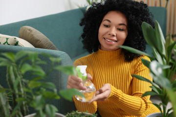 Canvas Print - Happy woman spraying beautiful potted houseplants with water indoors