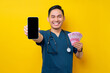 © Bangun Stock Photo - Cheerful young Asian male doctor or nurse wearing blue uniform holding cash money and showing a mobile phone blank screen isolated on yellow background. Healthcare medicine concept