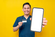 © Bangun Stock Photo - Smiling young Asian male doctor or nurse wearing blue uniform holding credit bank card and showing mobile phone blank screen isolated on yellow background. Healthcare medicine concept