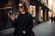 © GustavsMD - Happy beautiful elegant girl in a black dress, using a mobile phone, holding shopping bags. Black Friday, shopping