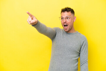 Wall Mural - Young caucasian handsome man isolated on yellow background pointing away