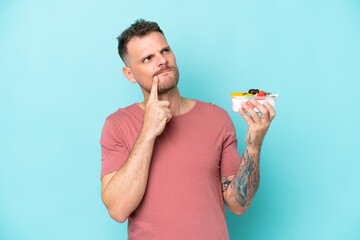 Wall Mural - Young caucasian man holding a bowl of fruit isolated on blue background having doubts while looking up