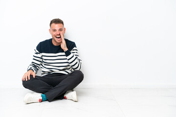 Wall Mural - Young man sitting on the floor isolated on white background shouting with mouth wide open