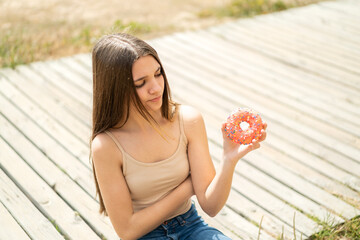 Poster - Teenager girl holding a donut at outdoors with sad expression