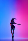 Beautiful female dancer wearing black and high heels while performing pole dance tricks in gradient neon light