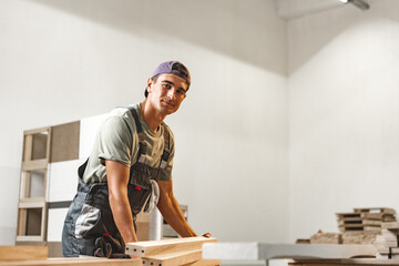 Wall Mural - Young carpenter man looking and choosing wood plank at workshop in carpenter wood factory