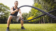 Handsome young man in sportswear doing workout ussing battle ropes in park