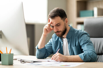 Aufkleber - Focused young businessman sitting at desk in office and writing in notepad