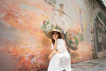 Portrait of Asian Vietnamese woman with Vietnam dress and straw hat with Graffiti in Hanoi, vietnam art drawing on wall. Urban city town. Street photography. People lifestyle.