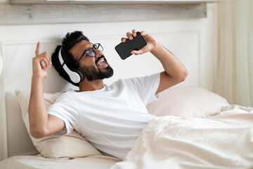 Sticker - Carefree Indian Man Man Listening Music On Smartphone And Singing In Bed