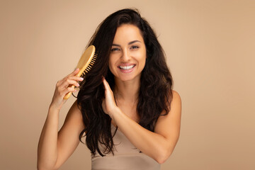 Cheerful indian woman combing beautiful dark long hair, studio background