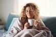 © id512 - beautiful young blond dreamy woman sitting on bed wrapped in a blanket drinking tea or coffee