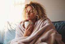 Beautiful Young Blond Dreamy Woman Sitting On Bed Wrapped In A Blanket Drinking Tea Or Coffee