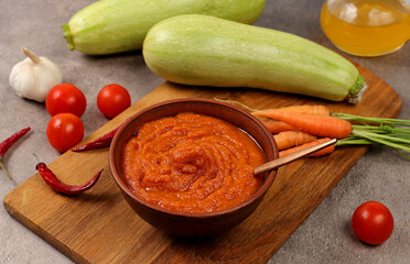 Wall Mural - Zucchini caviar with ingredients for cooking on a concrete table, the concept of home canning and harvesting vegetables, healthy organic food, tomatoes, zucchini, carrots and peppers 