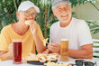 © luciano - Attractive cheerful senior couple sitting at pub restaurant table eating sandwiches on a sunny summer day while enjoying glasses of cold beer