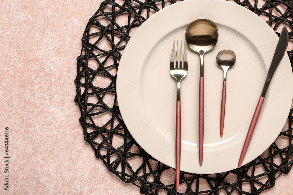 Black place mat with clean plate and cutlery on pink table