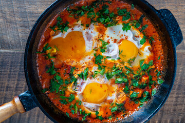 Wall Mural - Delicious shakshuka with eggs, tomato and parsley in a cast-iron pan, closeup, top view. Shakshuka - traditional israeli tomato stew with eggs