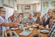 © Marko Geber - Group of senior friends having breakfast and using a smartphone in the morning in the kitchen