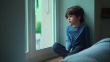 Bored Child Sitting Indoors By Apartment Window Looking Out From Second Floor Wanting To Go Outside, Little Boy With Sad Emotion