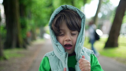 Portrait of a cute little boy standing outside at park smiling at camera and playing with hoodie jacket. Adorable expression