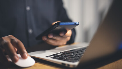 Hands using a smartphone and laptop simultaneously for secure login, highlighting the importance of multi-factor authentication.