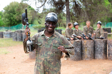 Canvas Print - Portrait of paintball player in camouflage and protective mask standing with gun after paintball match outdoors