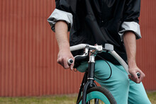 Unrecognizable Man In Casual Clothes Sitting On Bicycle And Holding Handlebars Against Brown Wall Background 