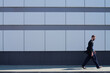 © TrueFrame Collective - Side view of young man in casual clothes walking by modern office building with glass facade