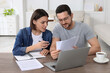 © New Africa - Young couple with papers discussing pension plan at wooden table indoors